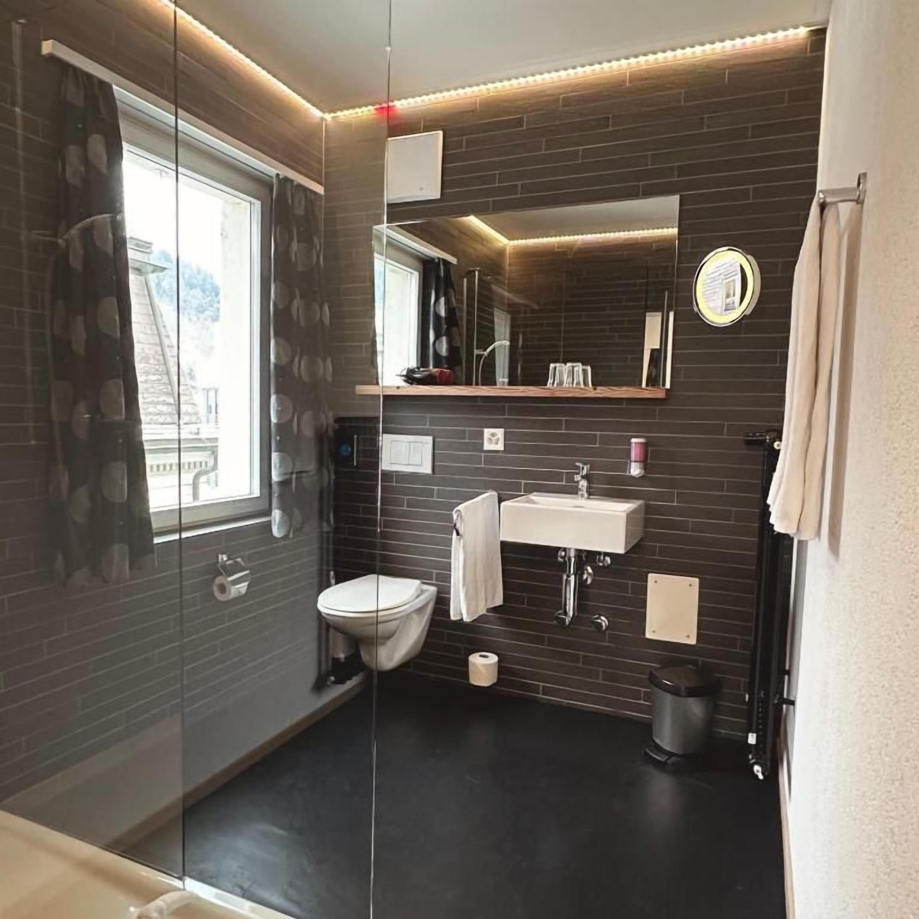 Un bagno moderno con pareti divisorie in vetro, un water, un lavandino e uno specchio.