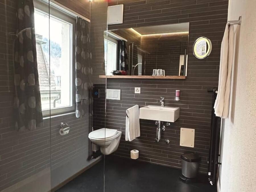 Un bagno moderno con pareti divisorie in vetro, un water, un lavandino e uno specchio.