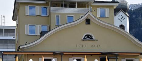 Un hotel con una torre de reloj, mesas al aire libre y un cartel que dice "HOTEL RATIA".