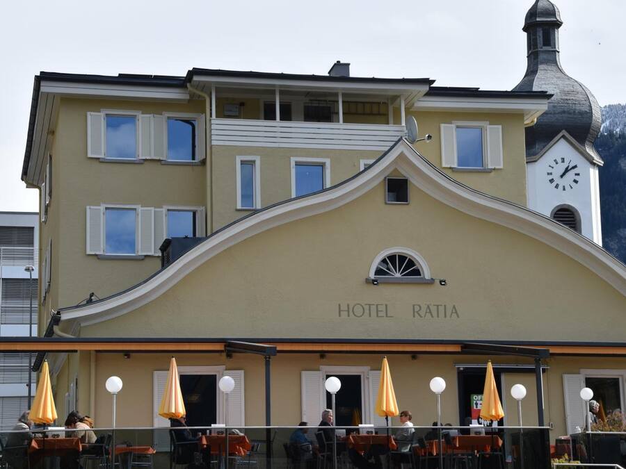 A hotel with a clock tower, outdoor seating, and a sign reading "HOTEL RATIA".