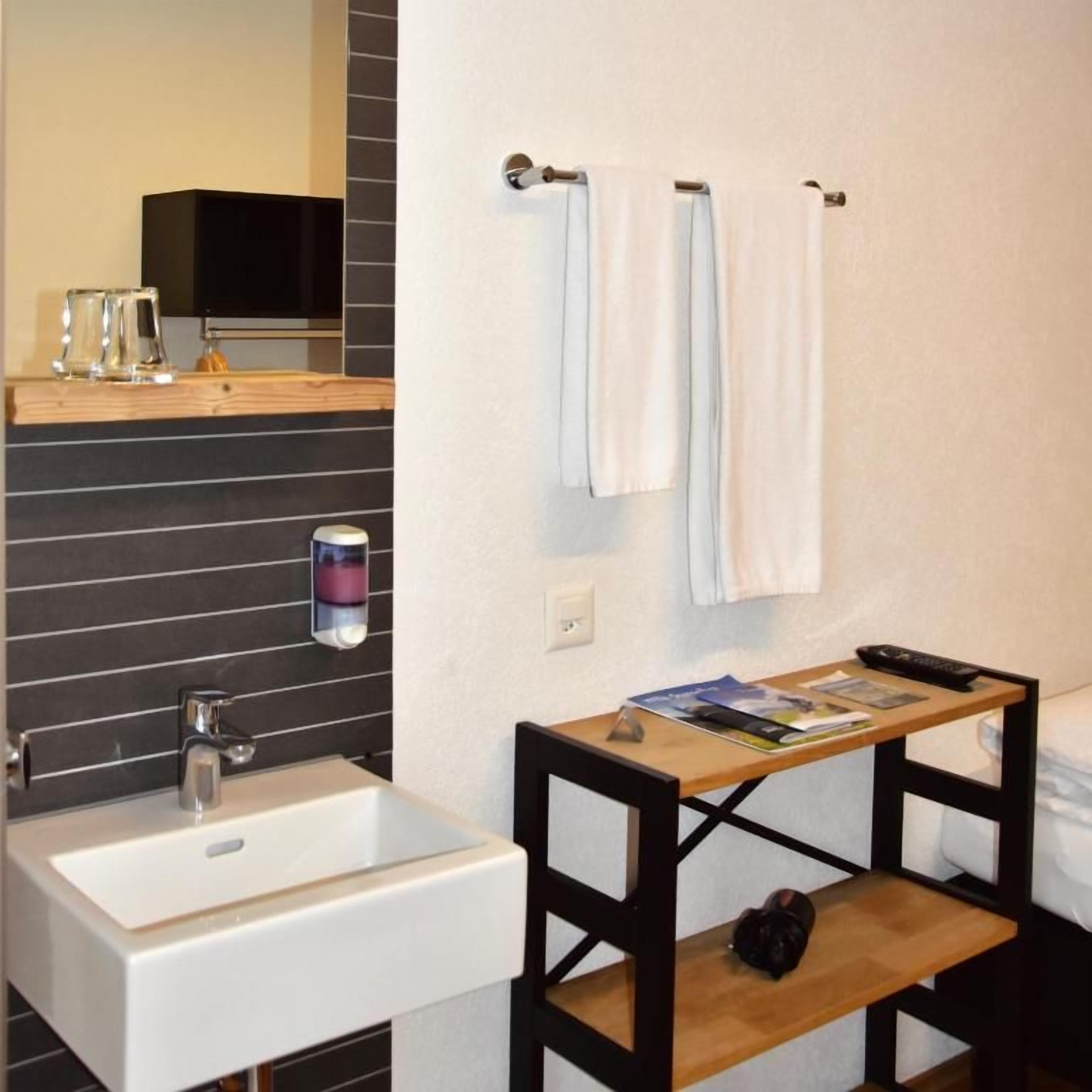 Un baño con lavamanos blanco, repisa de madera y toallero.