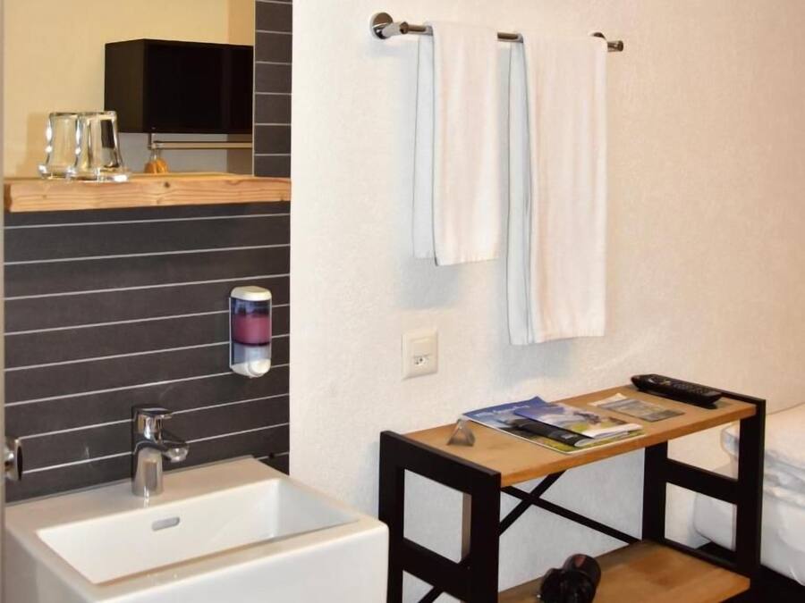 Un baño con lavamanos blanco, repisa de madera y toallero.