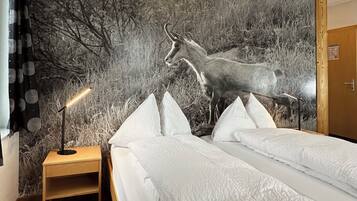 A room with a bed, a nightstand, a lamp, and a large wall mural of a deer.