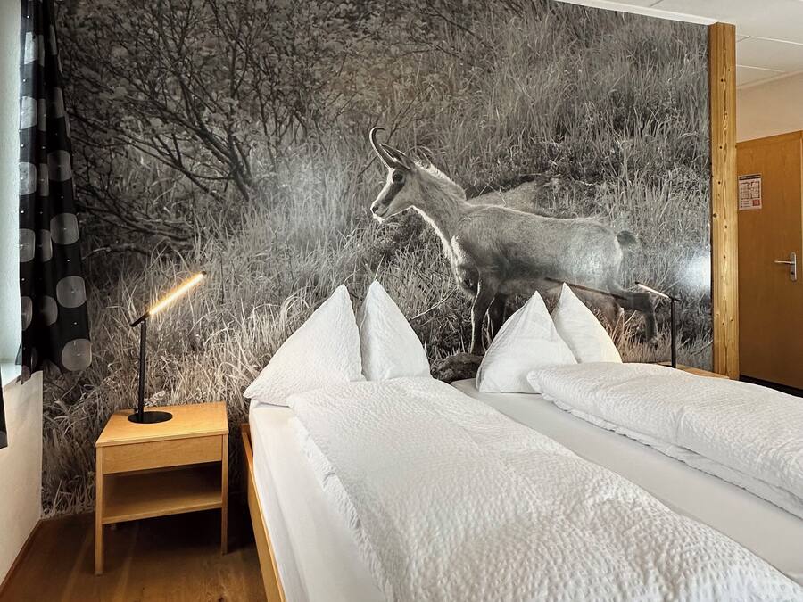 A room with a bed, a nightstand, a lamp, and a large wall mural of a deer.