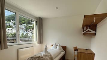 Un dormitorio con una cama de madera, un escritorio y una silla. Se ve una ventana con vistas a edificios.