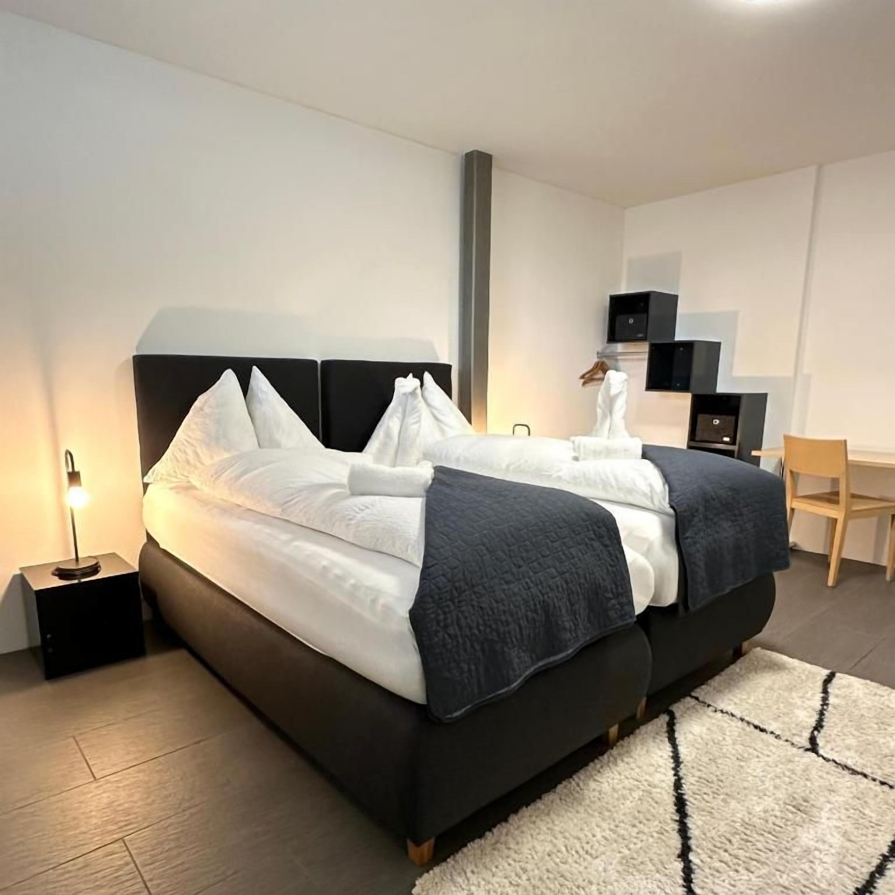 A modern bedroom with a large bed, bedside tables, a desk, and a chair.