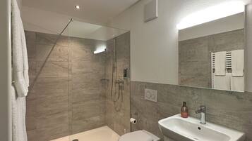 A modern bathroom with a glass-enclosed shower, a white toilet, and a sink with a mirror above.