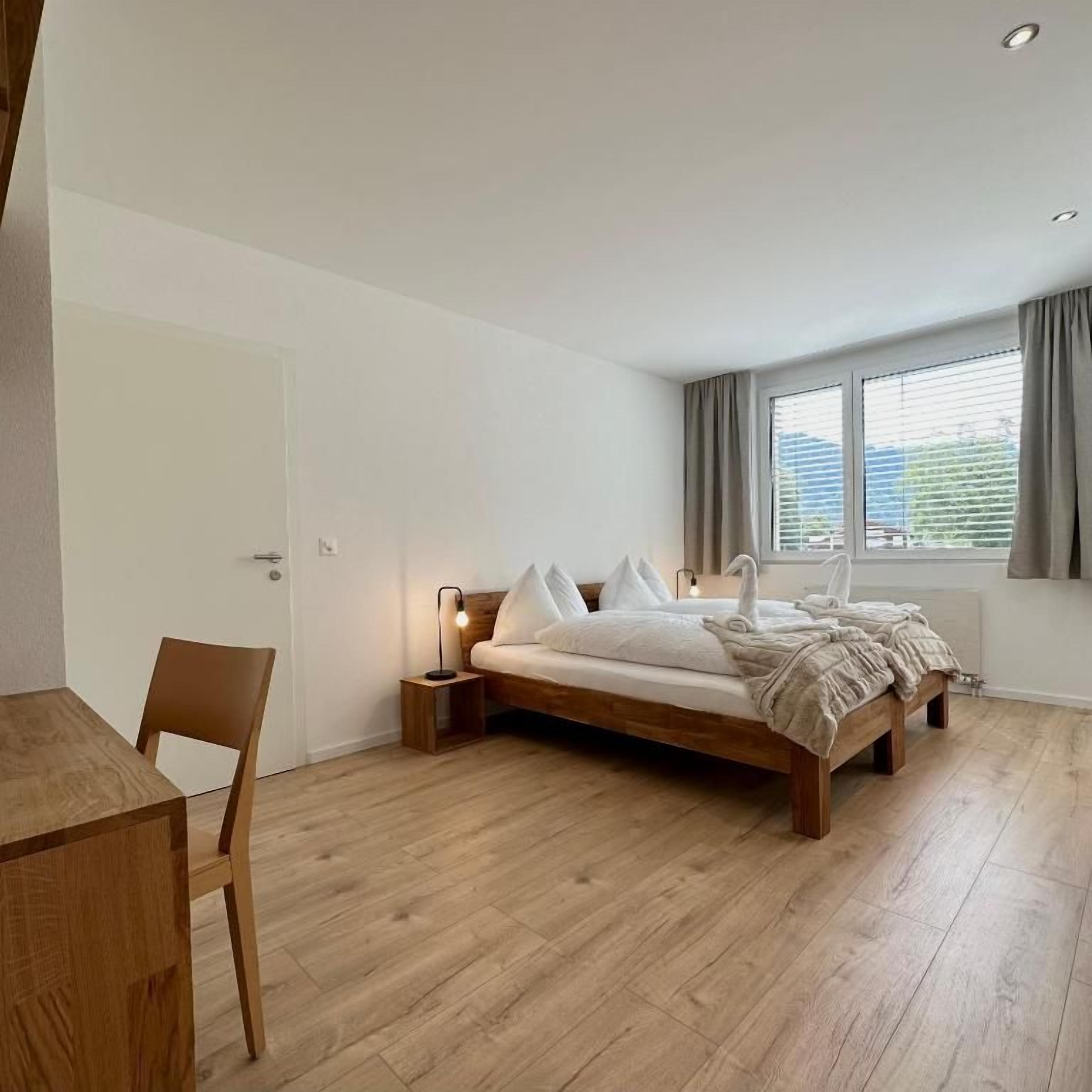 A bedroom with a wooden bed, a bedside table, a chair, and a window with curtains.
