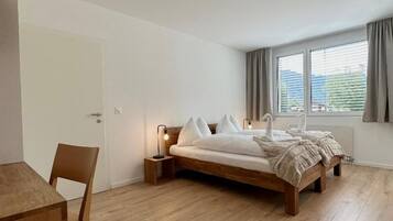 A bedroom with a wooden bed, a bedside table, a chair, and a window with curtains.