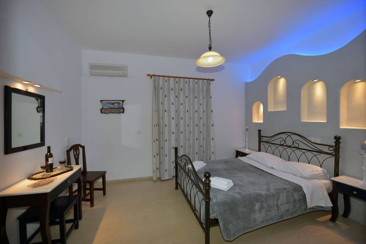 Un dormitorio con cama, escritorio, silla, ventana con cortinas e iluminación en la pared.