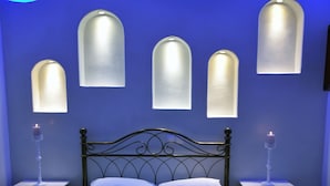 A bedroom with a bed, two nightstands, and wall-mounted sconces. - Sunflower Santorini (Santorini)
