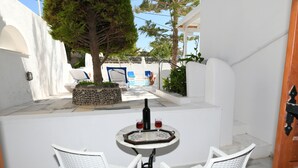 A white-walled outdoor area with a small pool, two white wicker chairs, a table with a wine bottle and glasses, and a stone planter. - Sunflower Santorini (Santorini)