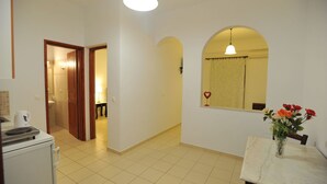 A spacious room with a tiled floor, a dining table with a vase of flowers, and a kitchen area with a kettle. - Sunflower Santorini (Santorini)