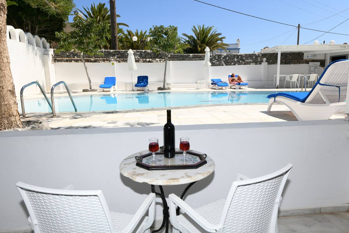 Un área junto a la piscina con una mesa, dos sillas y una botella de vino.