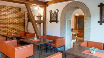 A restaurant with brick walls, wooden beams, and orange leather seating. Tables are arranged for dining.