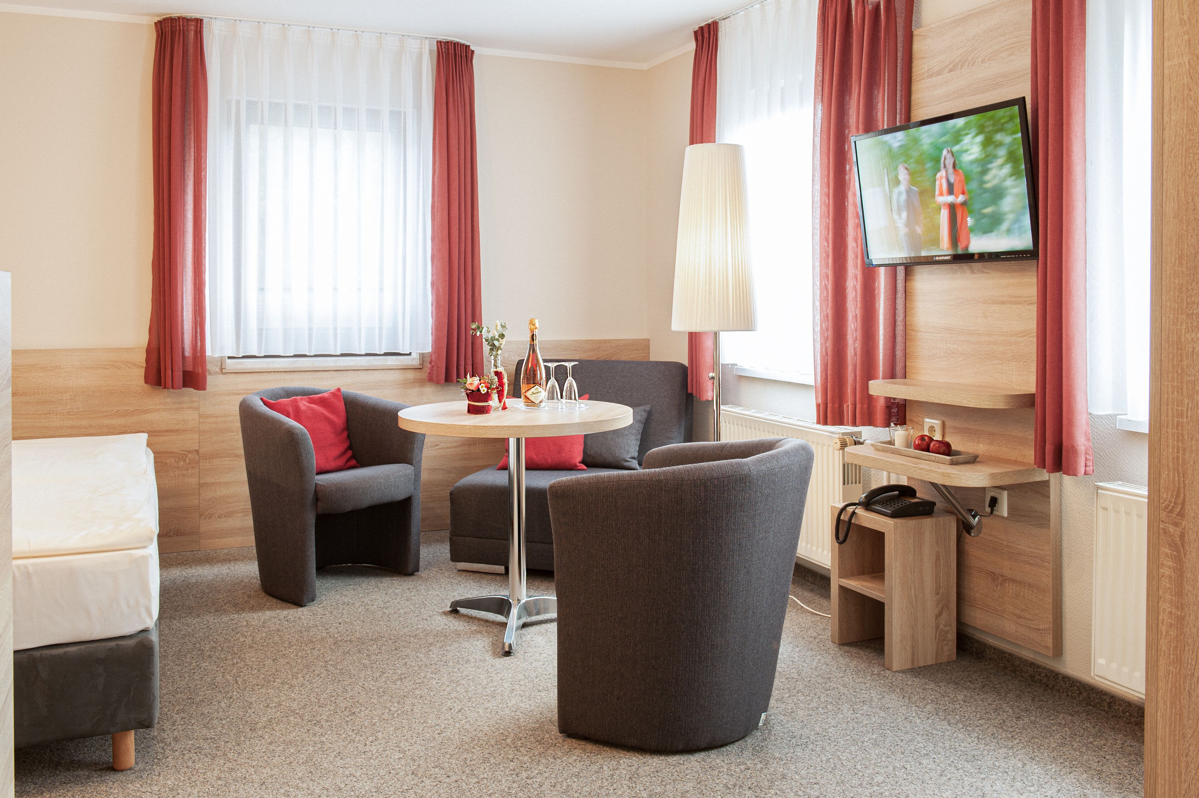 Ein Hotelzimmer mit Sofa, Sesseln, einem kleinen runden Tisch und einem an der Wand befestigten Fernseher.