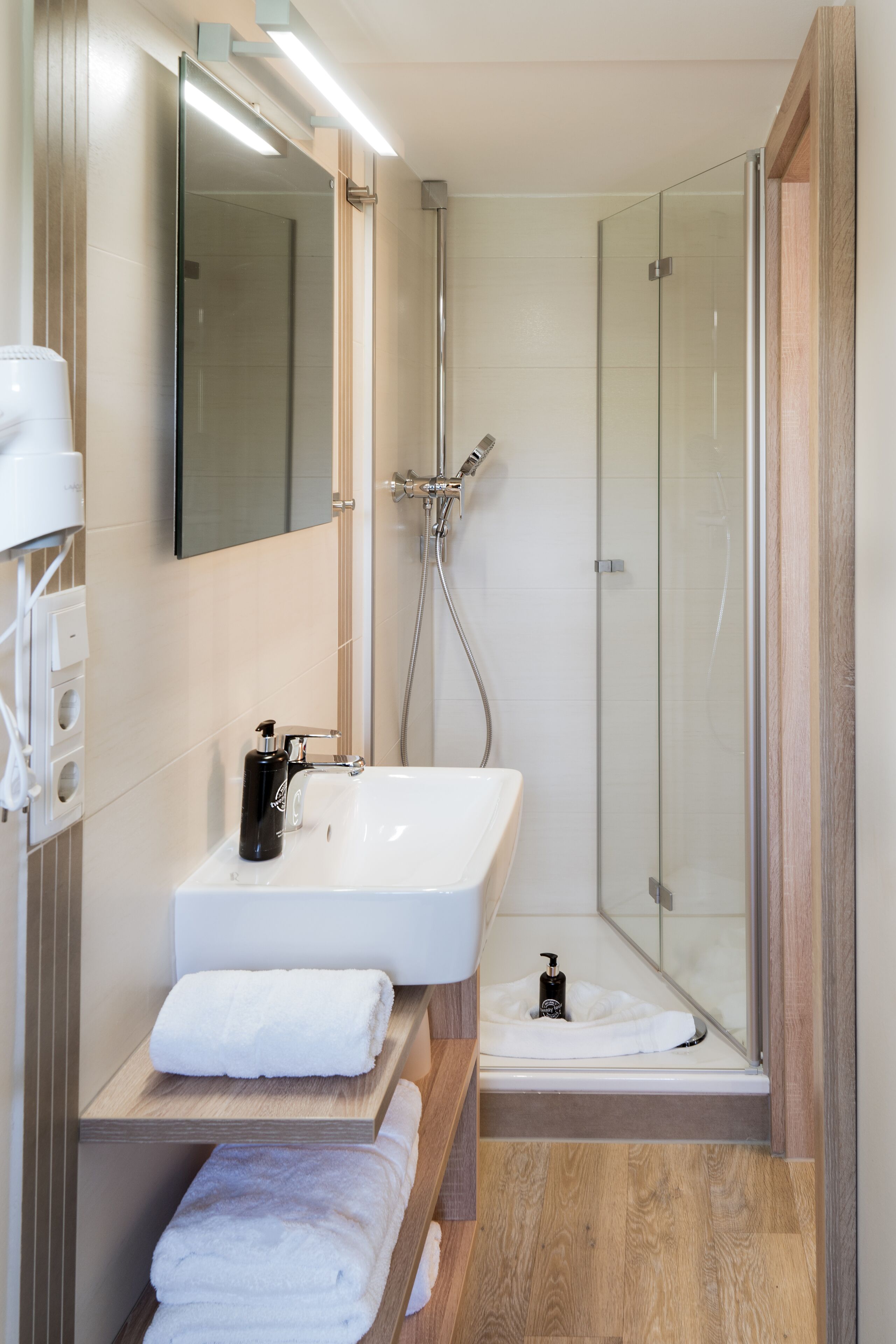 A modern bathroom with a glass shower enclosure, a white sink, and a wooden vanity.