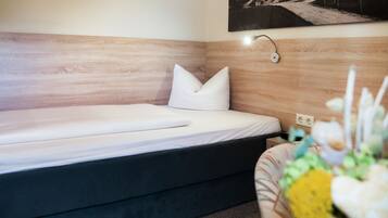 Una camera d'albergo moderna con una testiera in legno, un letto singolo con biancheria da letto bianca, un comodino e una lampada a parete.