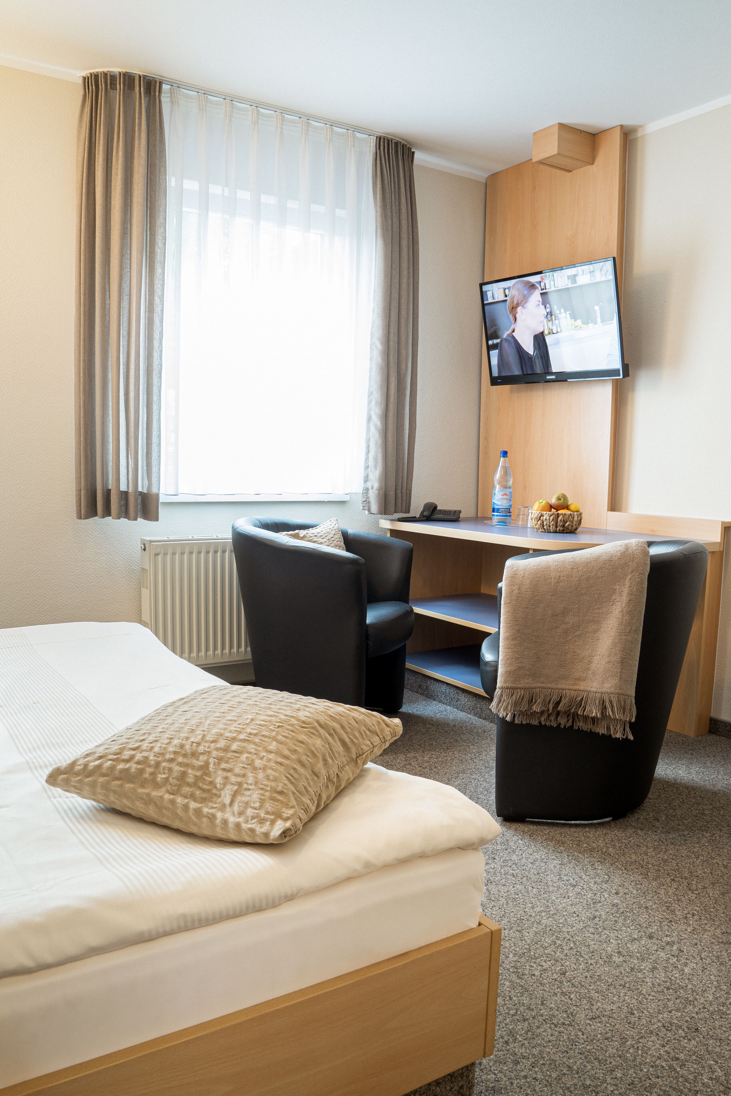 A hotel room with a bed, a desk, a chair, a television, and a window with curtains.