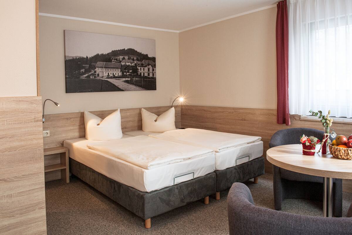A hotel room with a double bed, a small table with fruit, and a painting on the wall.