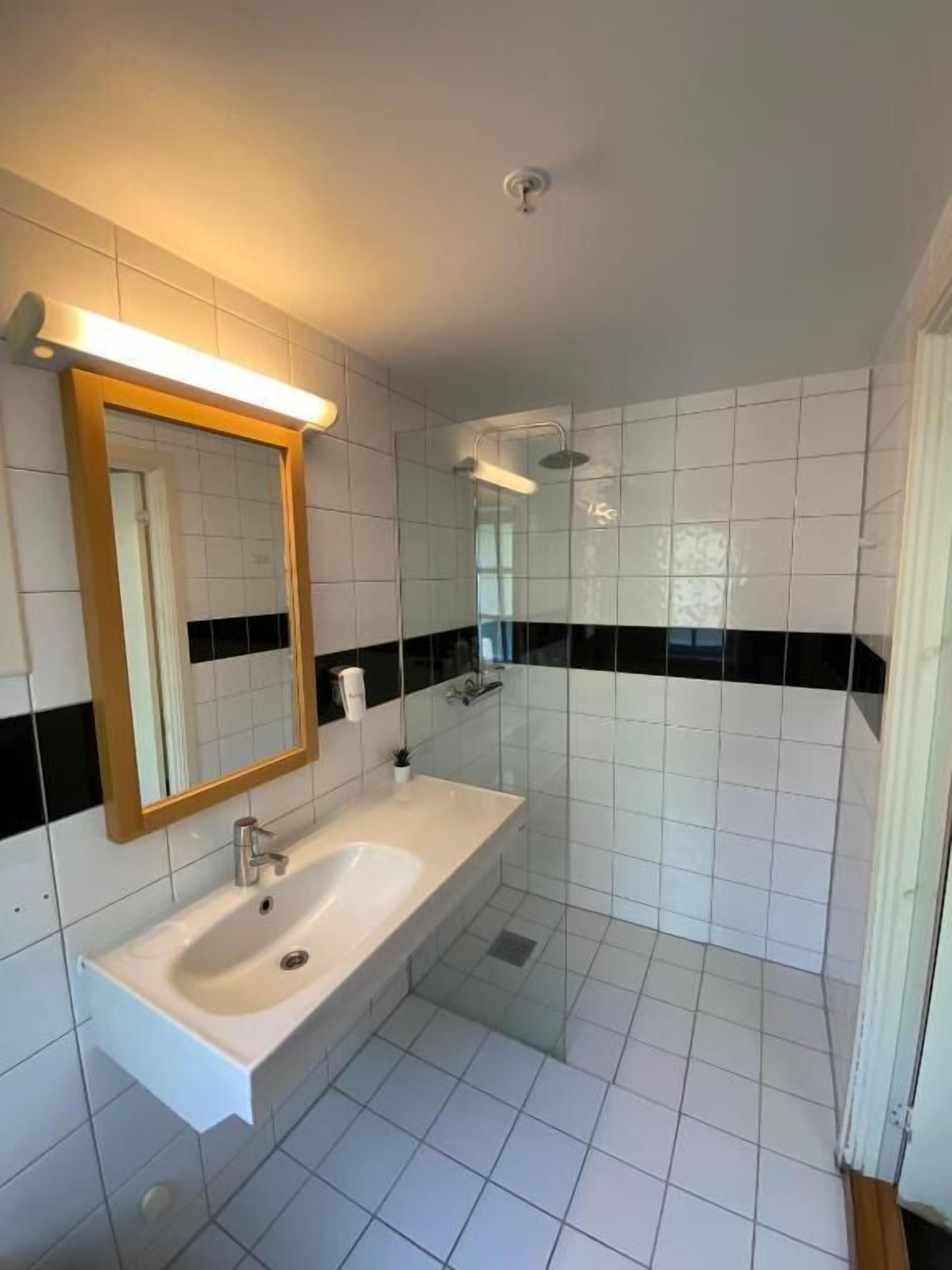 A bathroom with a white sink, a mirror, and a shower area.