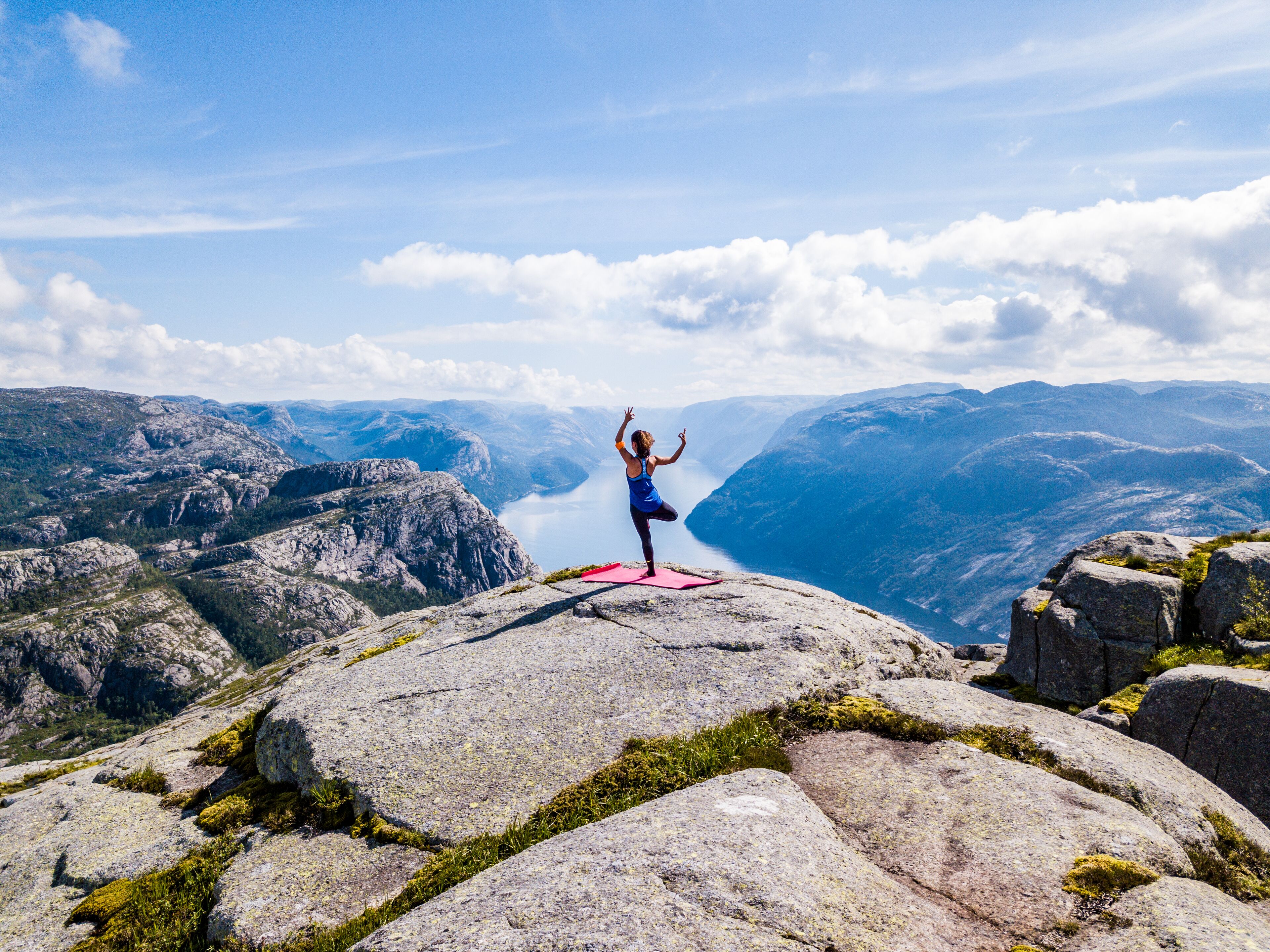 En person utövar yoga på en klippavsats med en vacker bergsvy i bakgrunden.