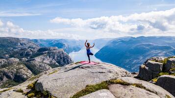 En person utövar yoga på en klippavsats med en vacker bergsvy i bakgrunden.