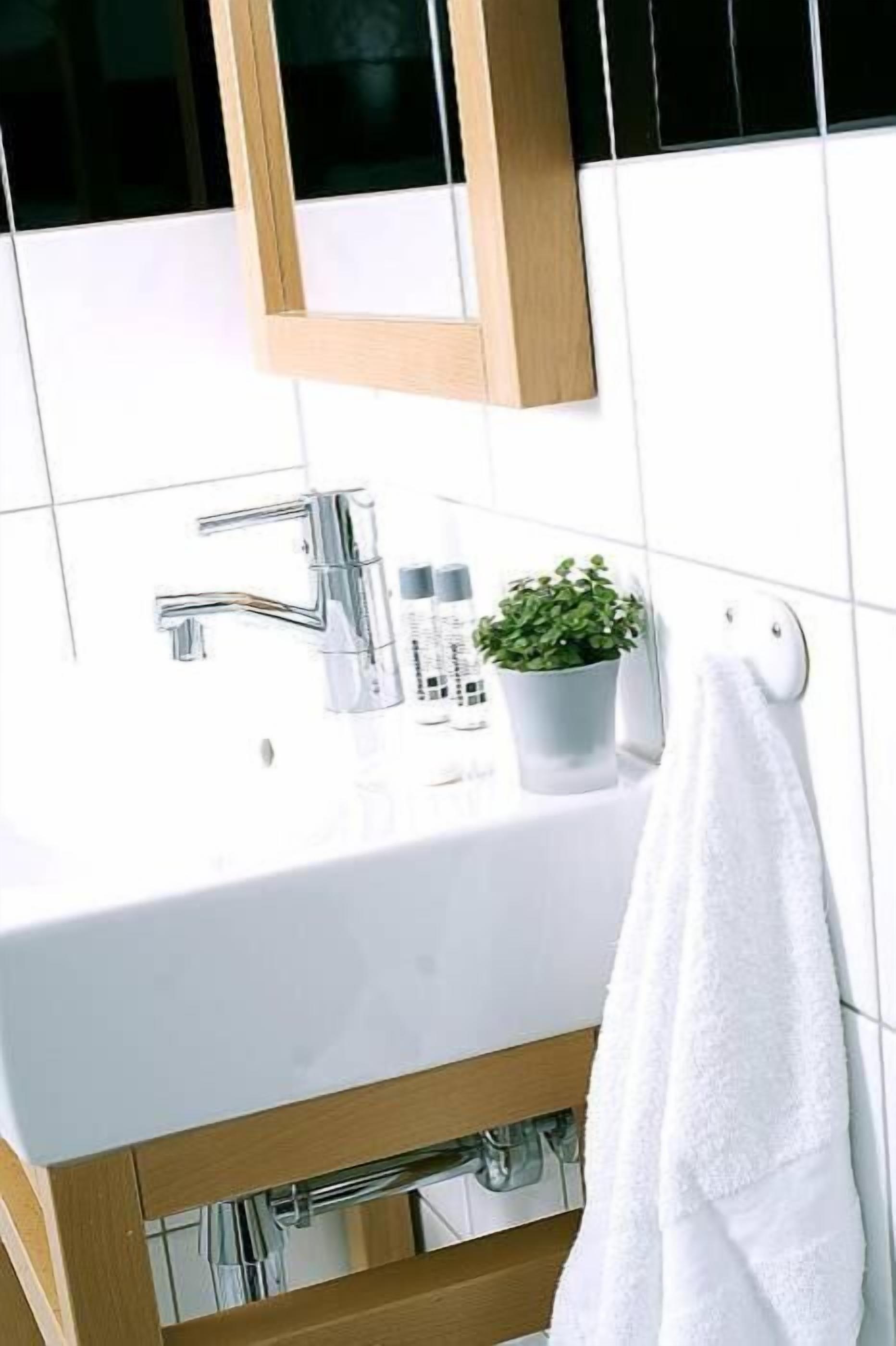 Ein Badezimmer mit einem weißen Waschbecken, einem chromfarbenen Wasserhahn und einem kleinen Topfpflänzchen.