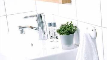 Ein Badezimmer mit einem weißen Waschbecken, einem chromfarbenen Wasserhahn und einem kleinen Topfpflänzchen.