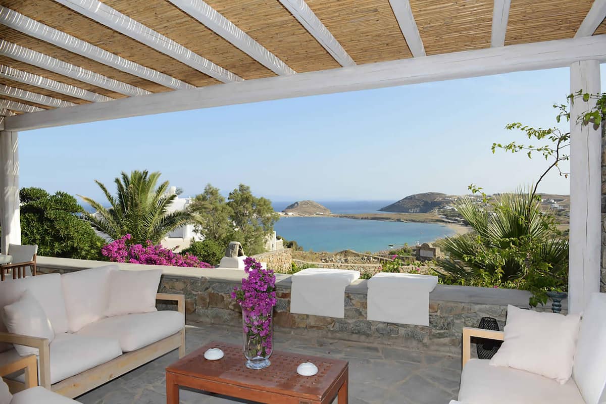 A covered outdoor seating area with a view of the sea and hills.