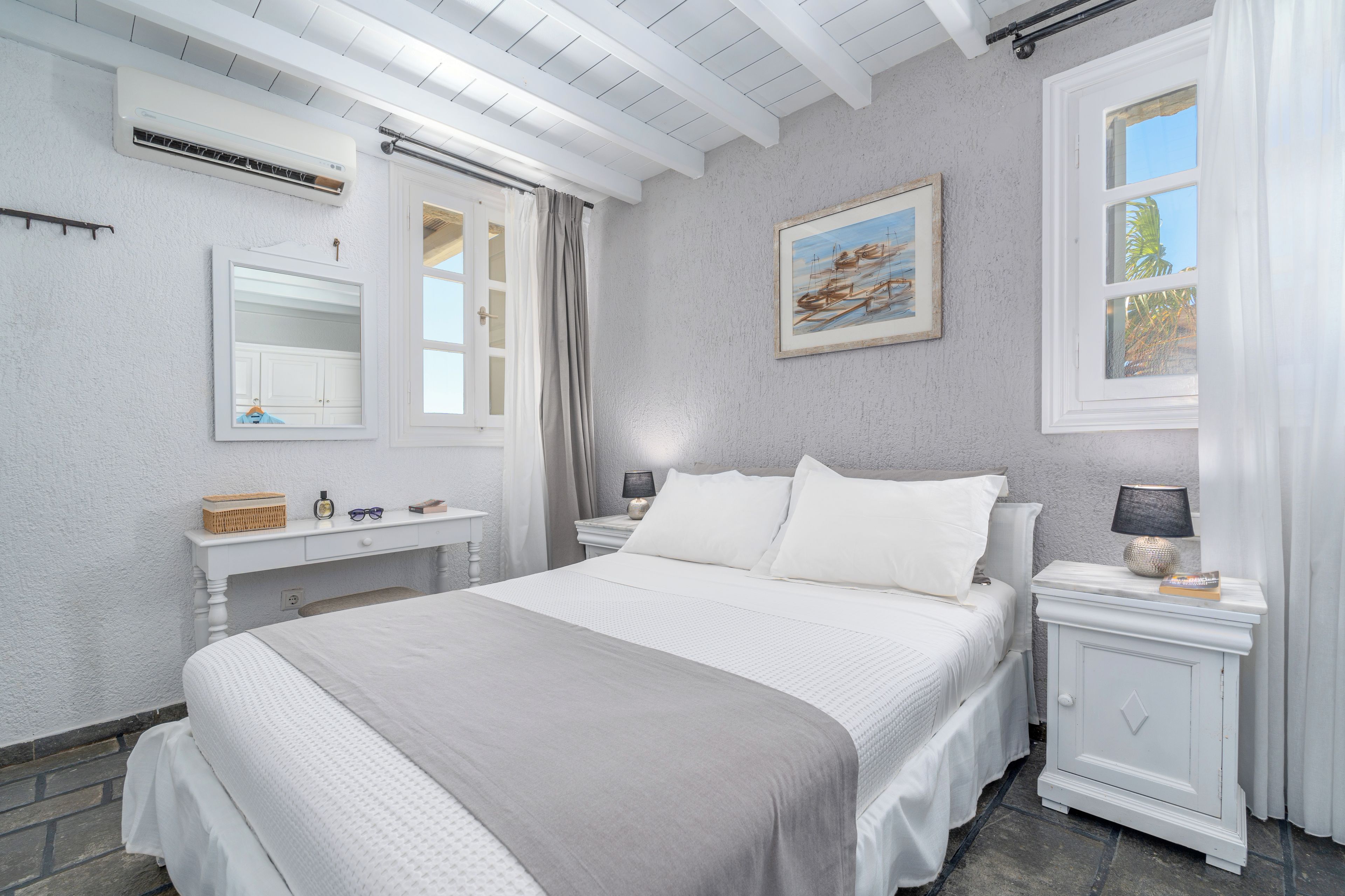 A bedroom with a bed, bedside tables, a dresser, a mirror, a painting, and a window with curtains.