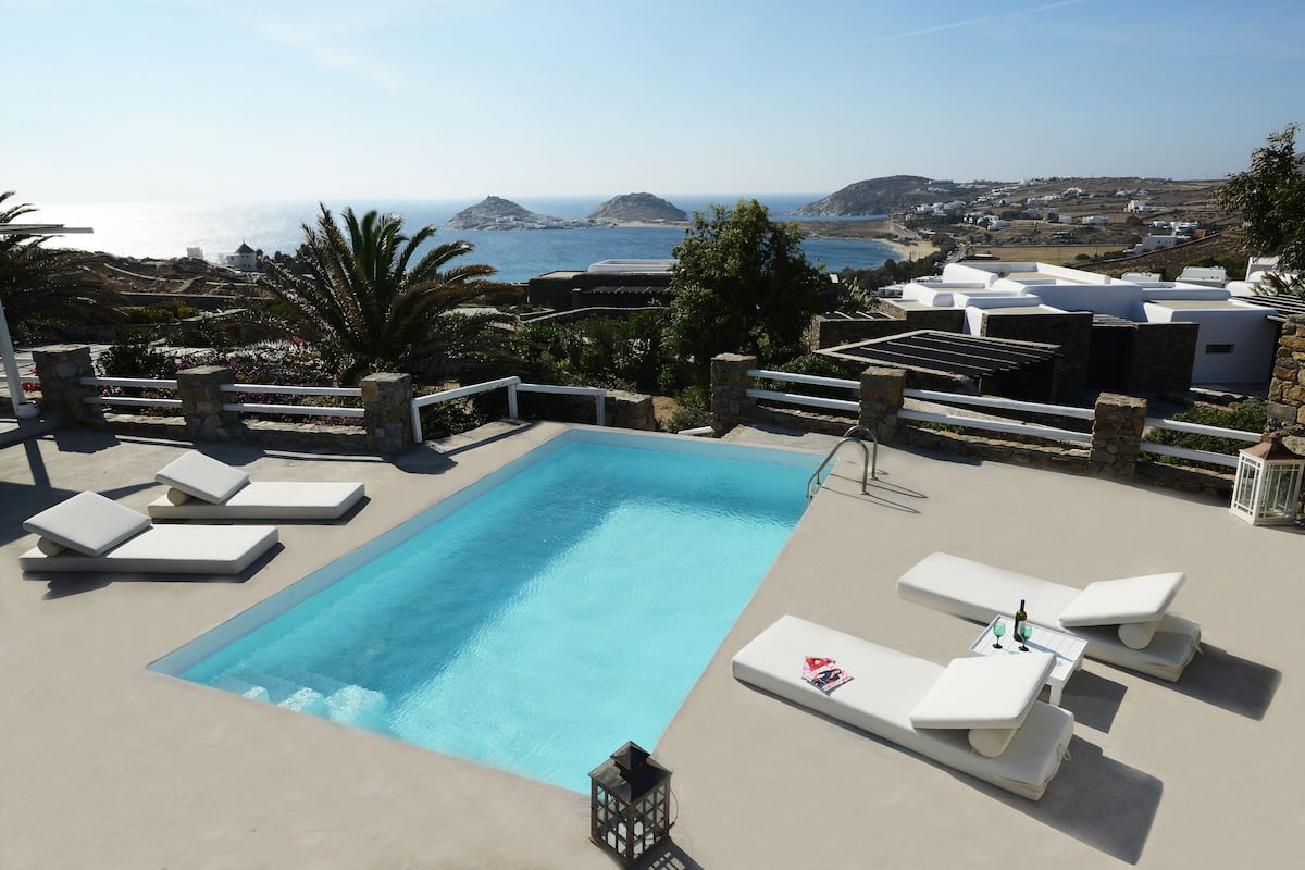 A swimming pool with lounge chairs, a stone lantern, and a view of the sea and hills.