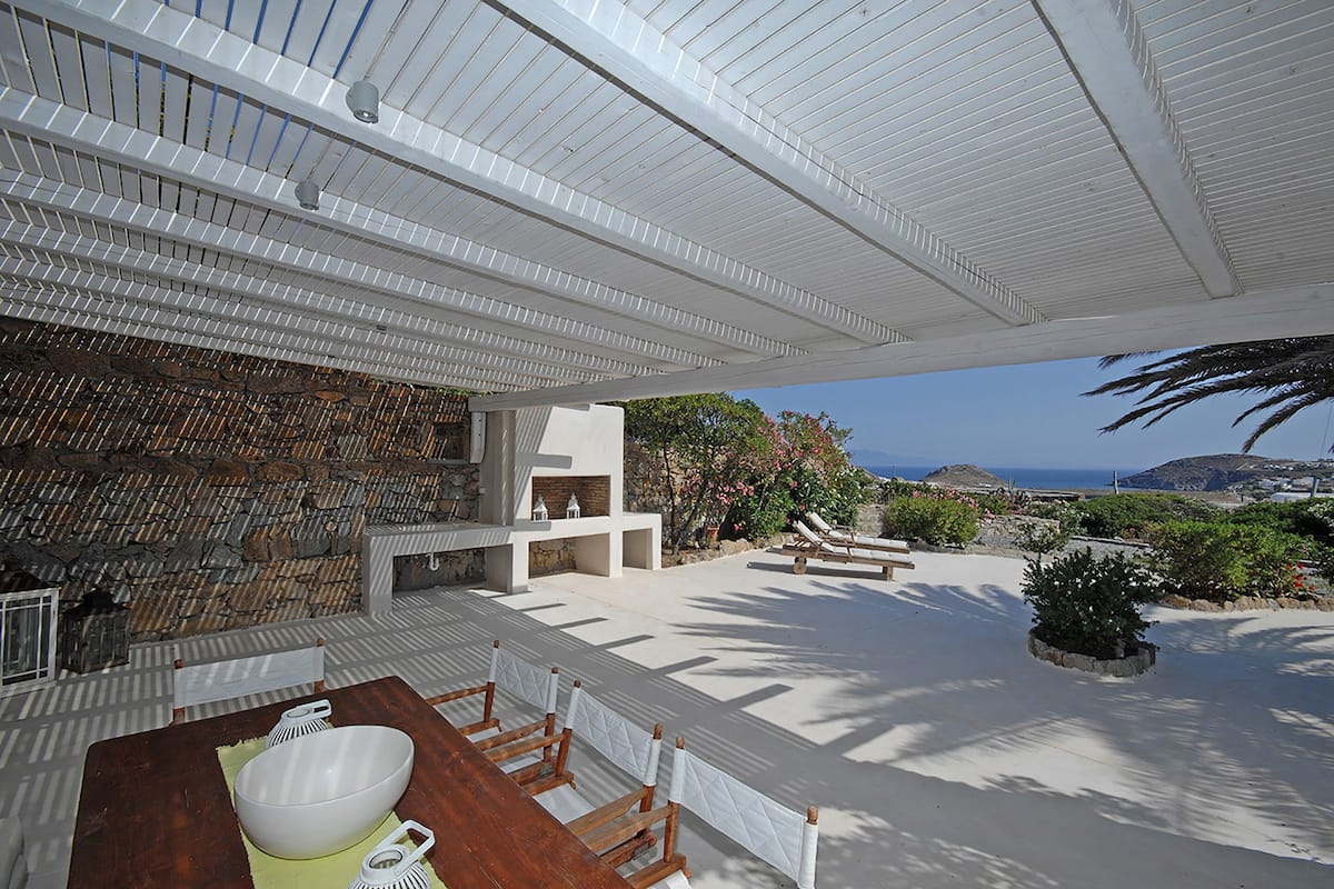 An outdoor dining area with a stone wall, a wooden table, and a view of the ocean.
