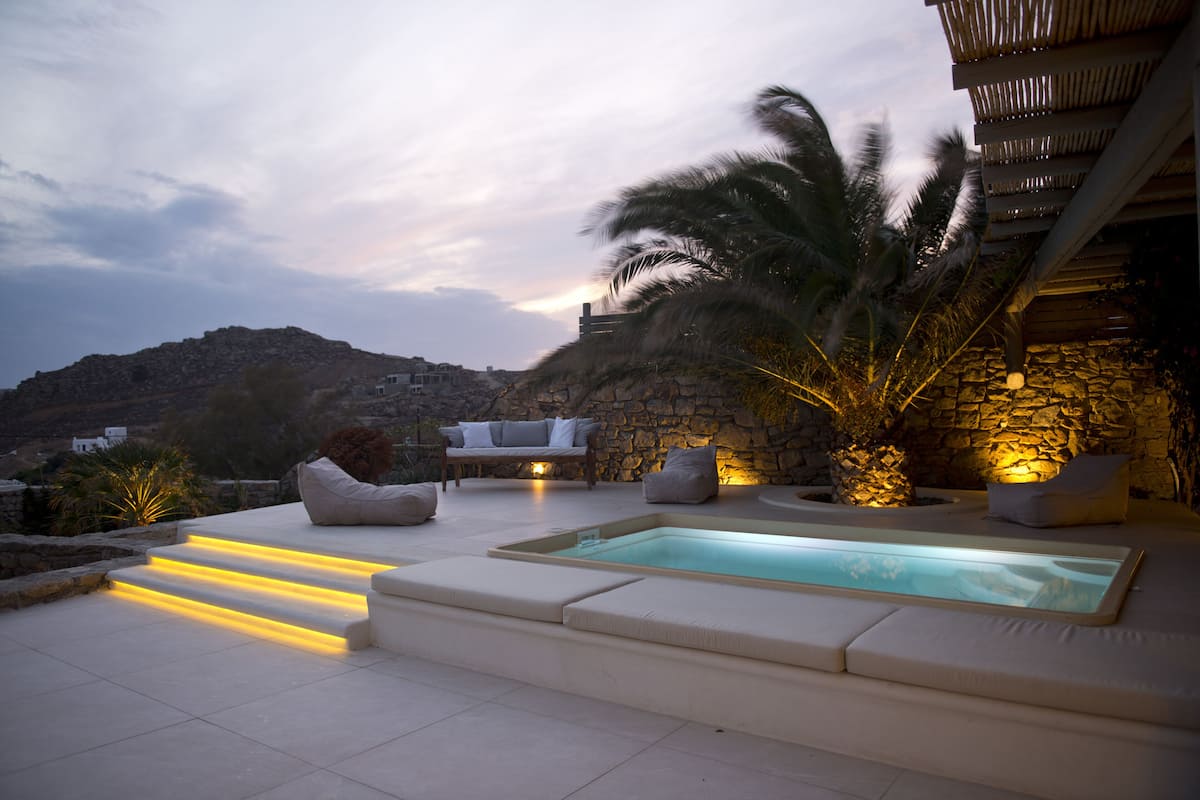 A rooftop pool area with a stone wall, a palm tree, and outdoor seating.