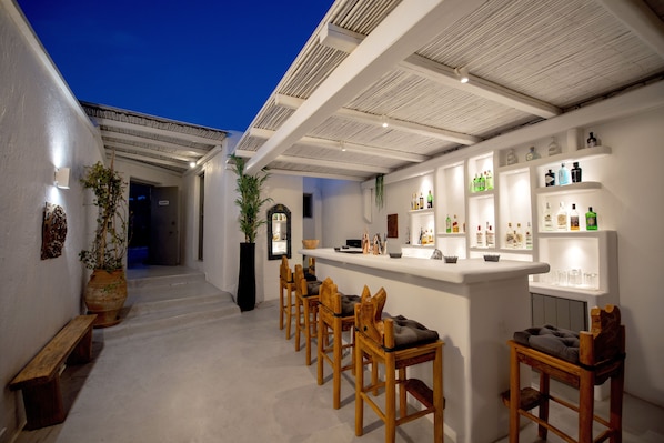 A bar area with wooden chairs and a counter displaying various bottles. - Thalasses Villas (Mykonos)