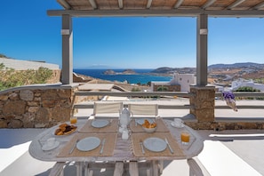 A table set for breakfast with a view of the sea and hills. - Thalasses Villas (Mykonos)