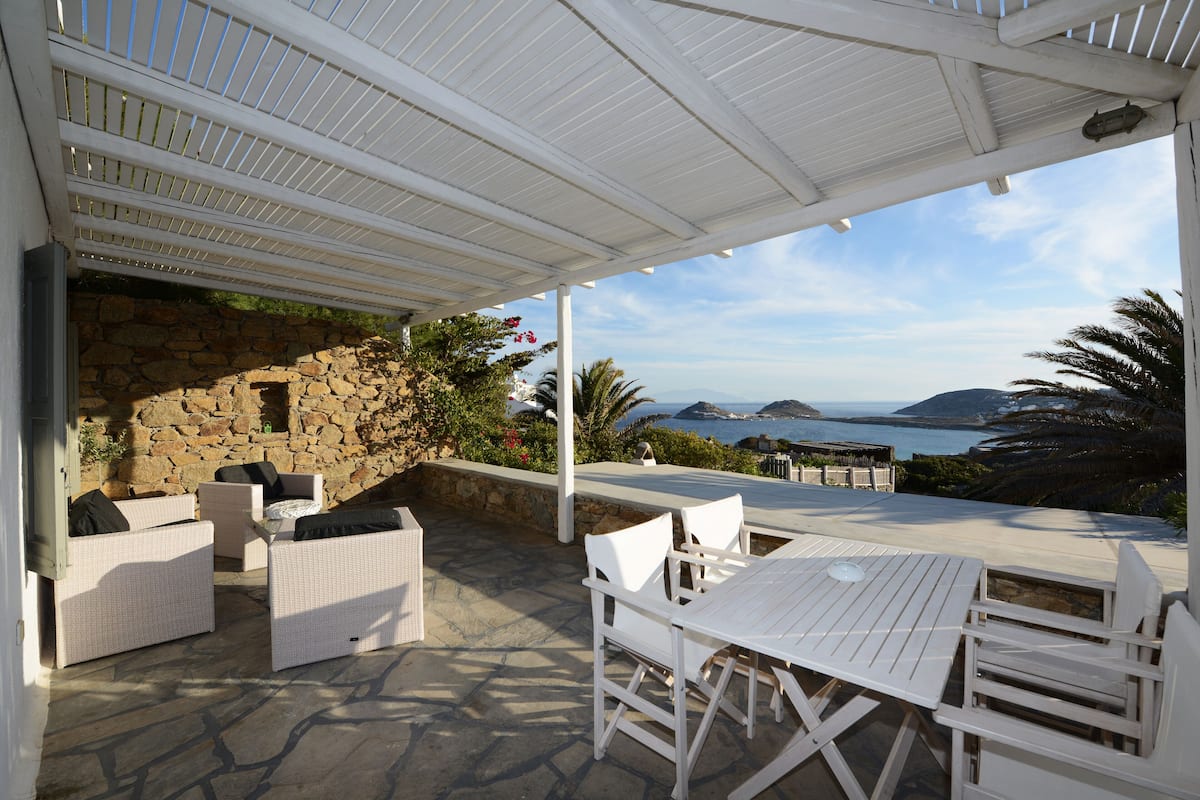 A covered outdoor seating area with stone walls and a view of the sea.