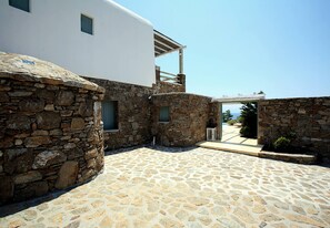 Une cour pavée de pierres, avec un bâtiment blanc, des murs en pierre et un espace extérieur abrité aménagé en coin salon.