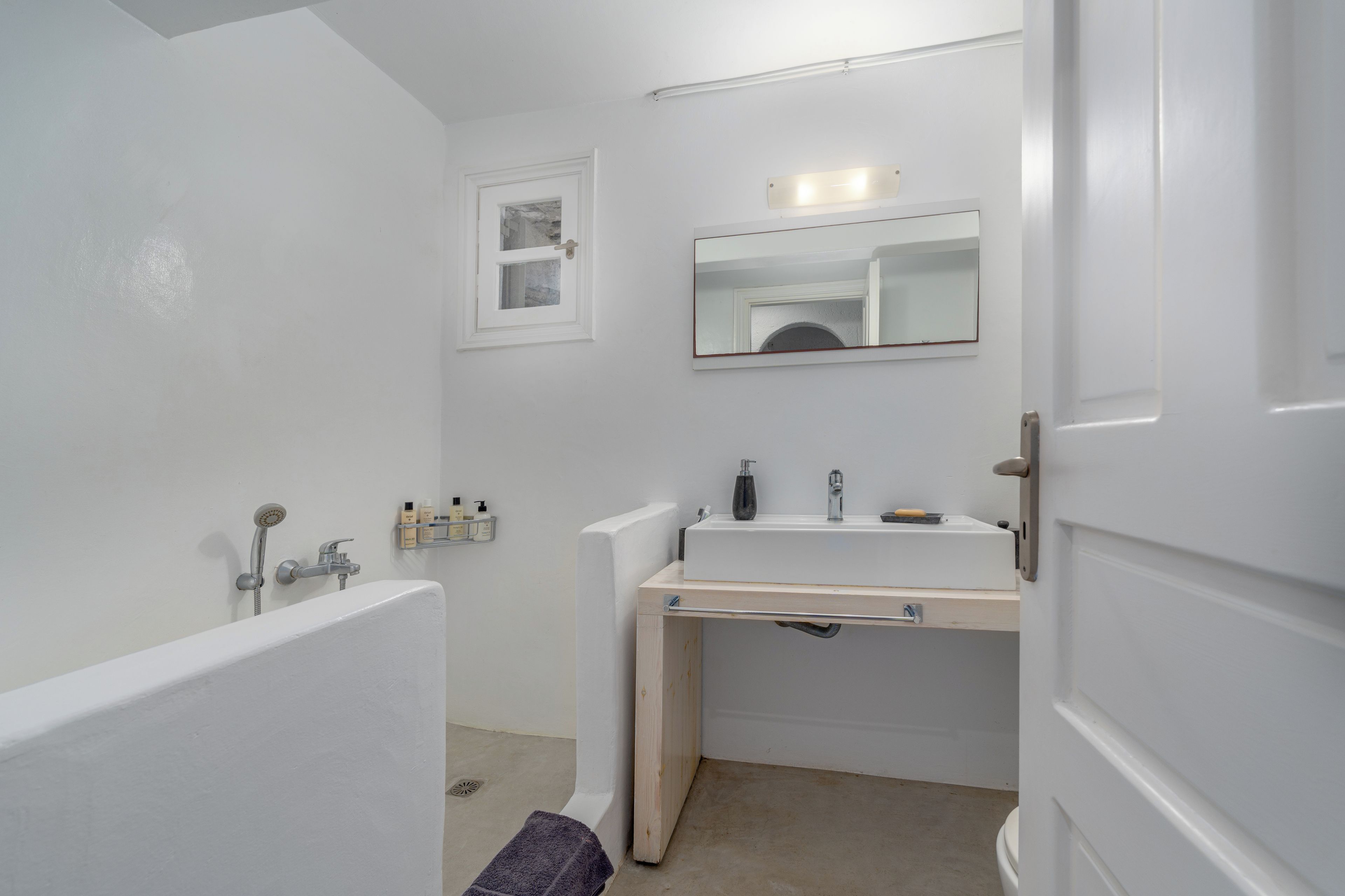 A bathroom with a bathtub, a sink, a mirror, and a small window.