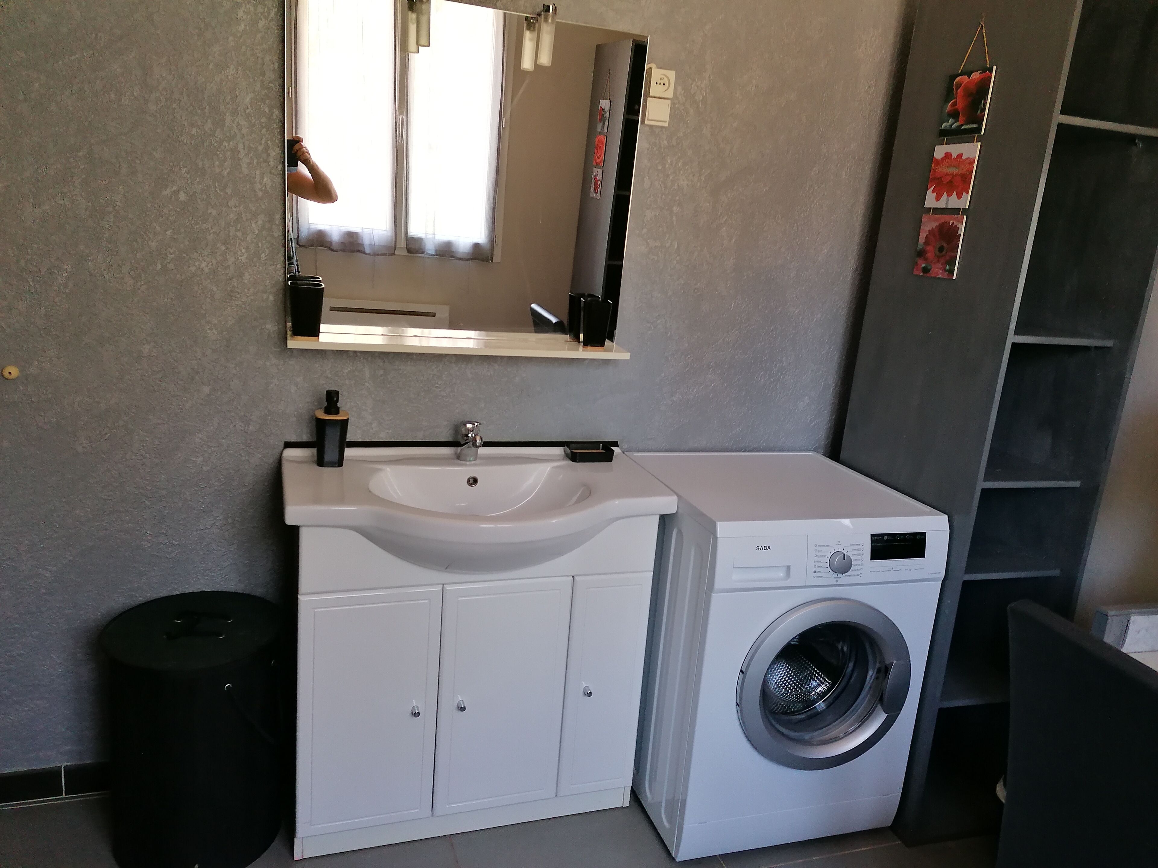 Ein kleines Badezimmer mit einem weißen Waschbecken, einem Spiegel und einer Waschmaschine mit Frontlader.