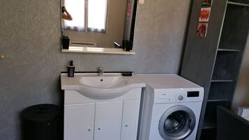 Ein kleines Badezimmer mit einem weißen Waschbecken, einem Spiegel und einer Waschmaschine mit Frontlader.