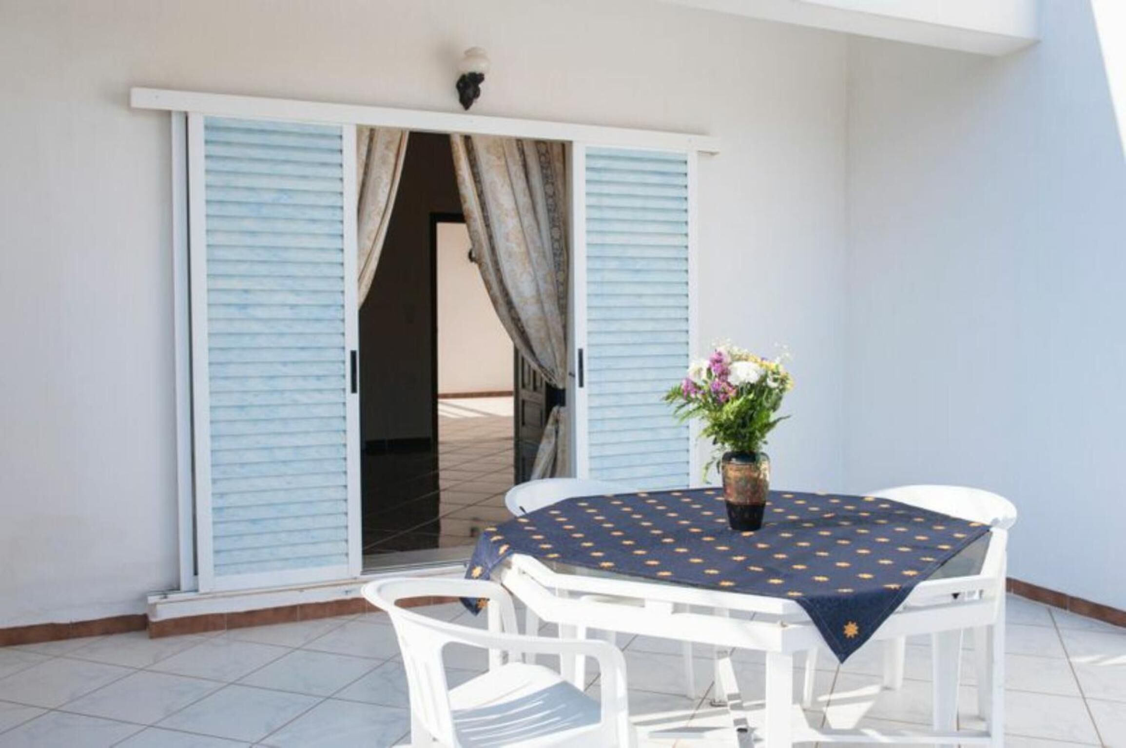 A balcony with a table and chairs, a potted plant, and blue shutters.