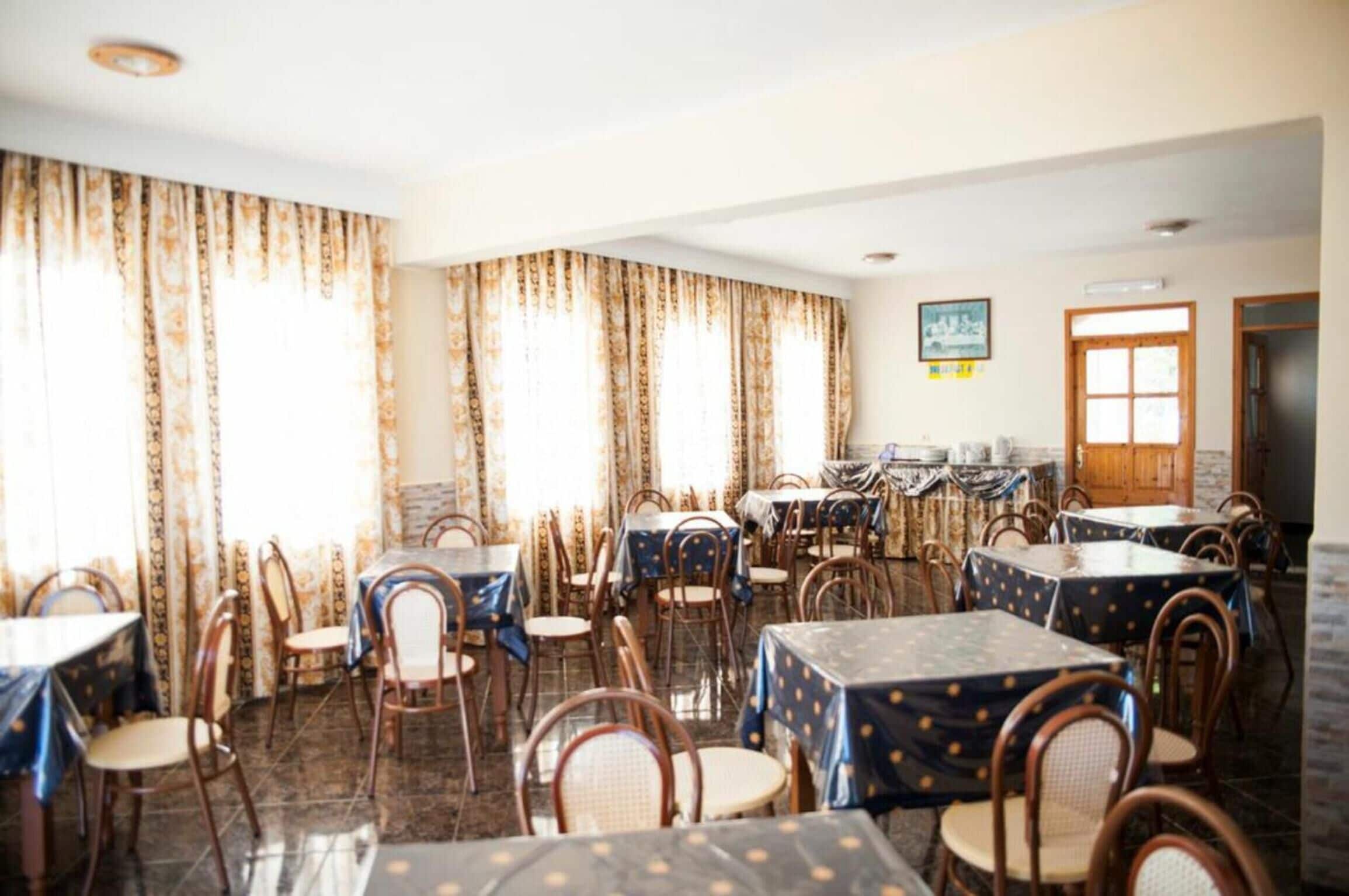 Un comedor con varias mesas y sillas, ventanas amplias con cortinas y una pared de ladrillo.