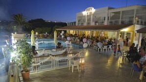 Un bar en la azotea con piscina, mesas al aire libre y un edificio con balcón.