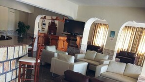 Una sala de estar con un sofá marrón, un televisor y una zona de bar con mostrador de piedra.