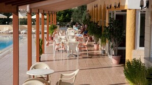Un patio al aire libre con mesas, sillas, una piscina y plantas en macetas.