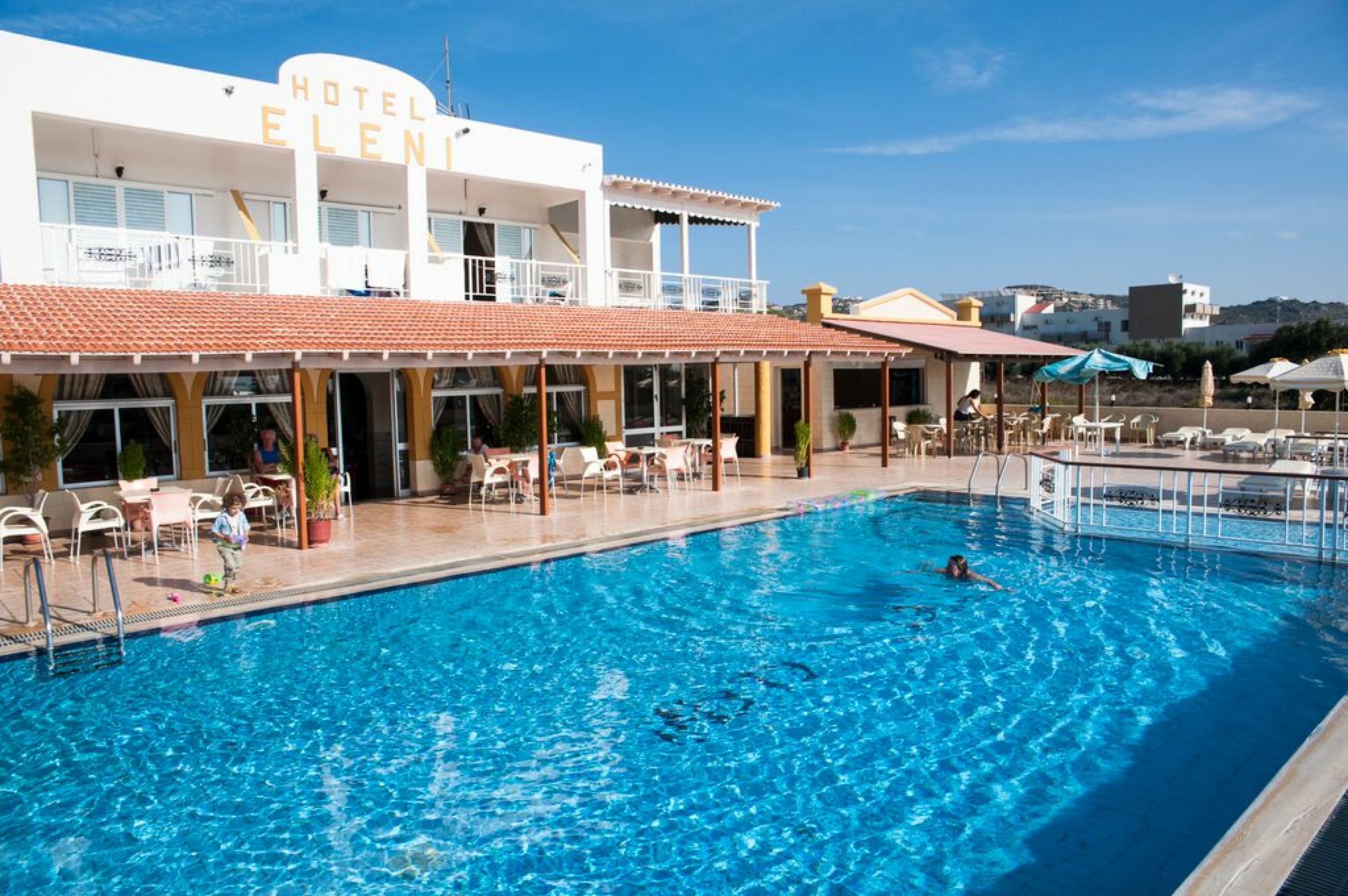 A hotel with a swimming pool, outdoor seating, and a clear view of the surrounding area.