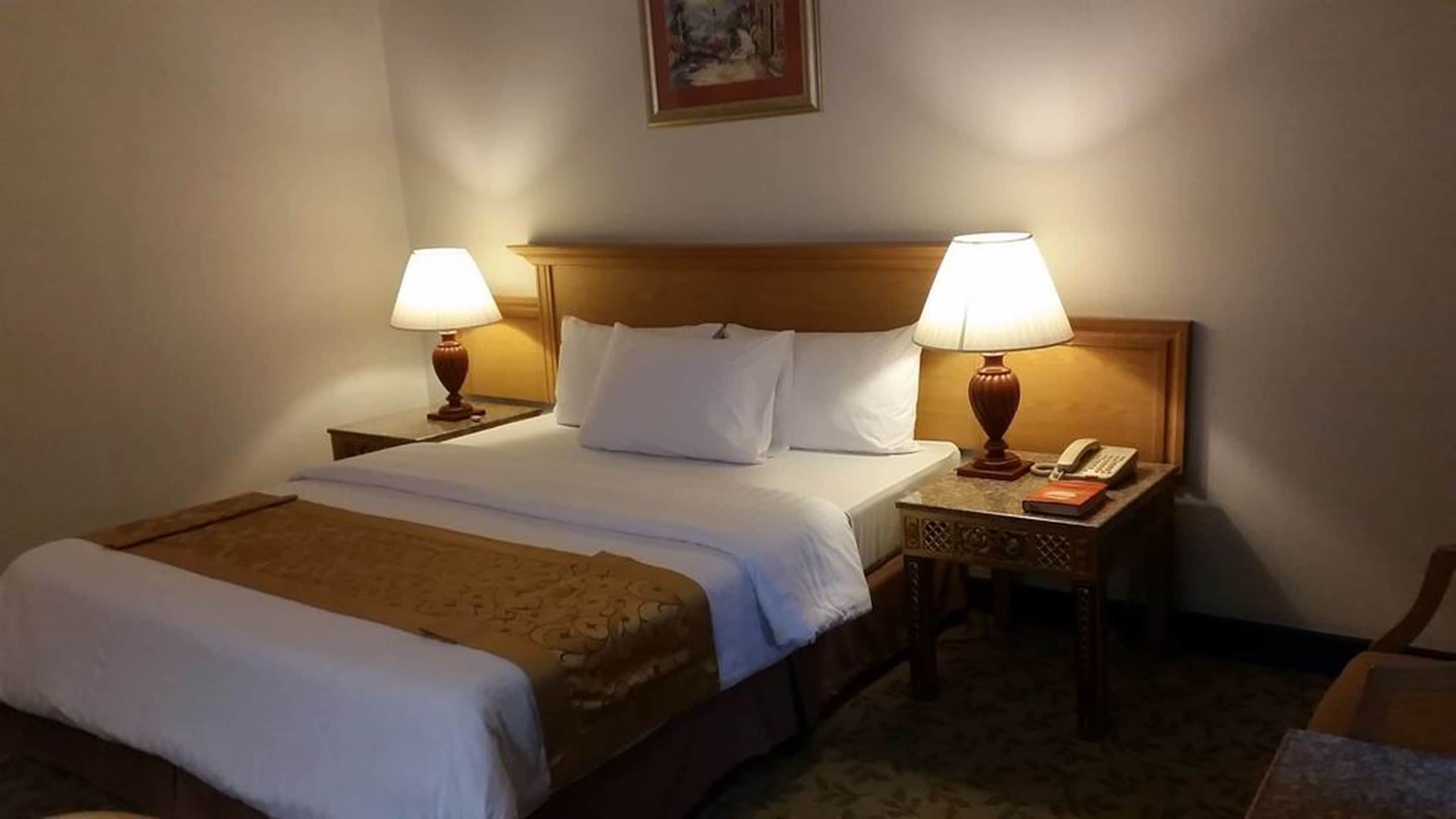 Une chambre d’hôtel avec un lit double, deux tables de chevet avec des lampes, un téléphone et un tableau au mur.