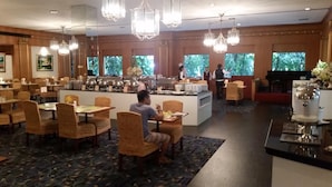 A hotel dining area with multiple tables and chairs, a buffet counter, and a coffee station. - Ariston Hotel (Bangkok)