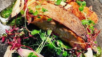A plate of food with a piece of salmon, greens, and sprouts.
